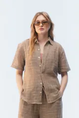 Camisa amplia y relajada de algodón liviano color blanco, de trama abierta y textura, con cuello camisero, mangas cortas y cierre de botones al frente.