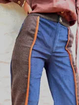 Pantalón de paño con silueta recta y levemente acampanada. Presenta un diseño de paneles combinados en azul marino y marrón, con detalles de vivos en cuero color naranja que recorren el largo de las piernas. Cuenta con cierre frontal y bolsillos laterales.