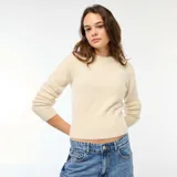 Sweater de punto fantasía en color beige, con cuello redondo y mangas largas. Presenta una textura suave y esponjosa, con un ajuste al cuerpo y puños acanalados.