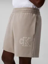 Short de jogging color beige, de tejido de punto de algodón acanalado, con cintura elástica, bolsillos laterales y trasero. Presenta logo CK bordado en blanco en la pierna izquierda.