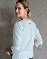 Remera blanca de manga larga con cuello en V y costuras decorativas en contraste. Incluye un lazo ajustable en el cuello con herraje metálico circular.