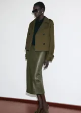 Chaqueta corta de doble botonadura en color verde militar, con cuello de solapa, bolsillos laterales, trabillas en los hombros y mangas largas con puños abotonados.