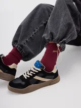 Zapatillas urbanas de cuero con paneles en gamuza negra y detalles en cuero color crema. Presentan suela de goma texturizada en tono marrón y cordones bicolores.