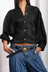 Camisa de lino blanca, de corte oversize, con mangas largas abullonadas, cuello mao y botones. Es más larga en la parte trasera e incluye un tajo en la espalda.