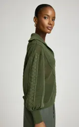Sweater de punto color verde militar, con cuello polo y escote en V, mangas largas abullonadas con puños ajustados y tejido con tramas geométricas combinadas.