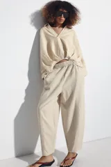 Pantalón de lino marrón oscuro, de corte barrel con pernera holgada que se estrecha hacia el tobillo, cintura elástica y bolsillos delanteros.