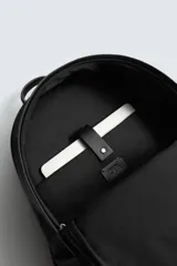 Mochila de tejido técnico en color negro, con compartimento principal con cierre de cremallera, bolsillo frontal con cierre y compartimento interior acolchado para dispositivos electrónicos. Cuenta con parte posterior acolchada, banda de sujeción para equipaje, asa de mano superior y correas de hombro ajustables.