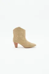 Bota corta estilo texano con taco medio de 6 cm. Confeccionada en cuero gamuzado, presenta recortes laterales que emulan la forma de una mariposa. Diseño de punta fina y caña media.