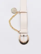 Cinto de cuero sintético color beige con hebilla metálica dorada y detalle de cadena colgante con dije circular.