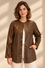 Camisa de cuero color marrón, de corte recto y largo medio, con cuello redondo a la base, cierre frontal con broches metálicos y bolsillos aplicados en los laterales.
