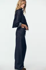 Pantalón de jean de tiro alto con corte de pierna ancha, cintura elástica con cordón ajustable y bolsillos laterales.