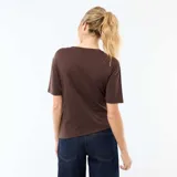 Camiseta marrón de manga corta con cuello redondo, diseño drapeado al frente y un botón metálico decorativo en la parte inferior.