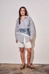 Camisa de corte oversize con diseño de rayas verticales en tonos azul y blanco. Presenta cuello clásico, cierre frontal con botones y mangas largas con puños abotonados.