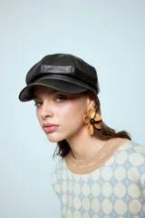 Boina estilo cap con visera, confeccionada en cuero vegano de color marrón oscuro. Presenta un diseño estructurado con costuras visibles en la parte superior.
