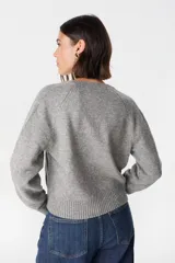 Saco tipo cardigan de punto color crudo, con cuello redondo, cierre frontal de botones y mangas largas con puños acanalados.