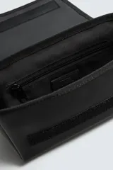 Bandolera negra con acabado engomado, compartimento principal con cierre de solapa y bolsillo con cremallera. Interior con bolsillo con cremallera. Asa de hombro ajustable.