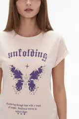 Remera rosada de manga corta, con diseño holgado y estampado frontal de mariposa y texto en tonos morados.