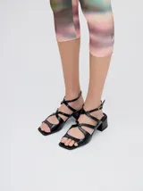 Sandalias de cuero con acabado charol color bordó, con punta cuadrada, tiras onduladas en el empeine y correa ajustable con hebilla en el tobillo. Cuentan con un taco bajo forrado.