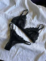 Conjunto de lencería de encaje negro, compuesto por un soutiene triangular y una bombacha colaless con tiras regulables.