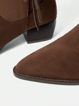 Botas de caña alta confeccionadas en gamuza color marrón, con diseño de flecos laterales y taco cuadrado de altura media.
