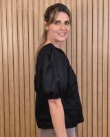 Blusa blanca de lino, con cuello redondo y mangas cortas abullonadas con frunces en los hombros.