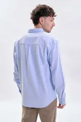 Camisa de manga larga confeccionada en tejido oxford color celeste, con cuello abotonado, cierre frontal de botones y bolsillo en el pecho.