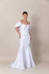 Vestido blanco de tafeta, strapless, con detalle de broche bordado en el escote. Presenta cinta trenzada en la espalda para ajustar y mangas caídas removibles. Vestido con cola.