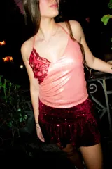Top halter escote en V de color rosado con acabado brillante, tirantes finos que se atan al cuello y un aplique de encaje rojo con bordados dorados en el lateral derecho del pecho.