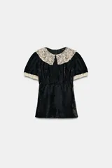 Camisa de terciopelo negro con cuello solapa grande en crochet color crema y detalles de crochet en los bordes de las mangas cortas. Presenta un diseño entallado con cierre de cremallera en la espalda.