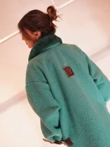 Buzo color crudo con cuello de piel sintética color crema, abertura parcial con cierre de cuero marrón y hebilla dorada, puños con ajuste de cuero marrón y bolsillos laterales.