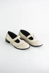 Zapato tipo guillermina estilo oxford, confeccionado en cuero color crema. Presenta detalles de perforaciones decorativas en la puntera, cierre con tira y hebilla metálica dorada, y un taco bajo cuadrado.