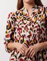 Blusa de gasa estampada con diseño geométrico multicolor, cuello a la base con escote en V y abertura frontal con botones. Presenta detalle de plisado en la parte delantera y mangas largas con sistema de ajuste mediante presilla y botón.