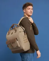 Mochila de diseño urbano en color beige con detalles en cuero sintético marrón. Cuenta con un bolsillo frontal con solapa y cierre de hebilla, asas superiores de mano y correas ajustables para hombros.