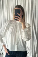 Camisa negra de manga larga con cuello alto tipo victoriano y detalle de fruncido en el pecho y puños. Presenta cierre frontal con botones y diseño de mangas abullonadas.