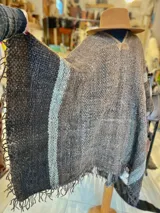 Poncho de lana virgen tejido en telar con diseño geométrico a rayas en tonos gris, marrón y celeste, con apliques de cuero en el escote y flecos en el ruedo.