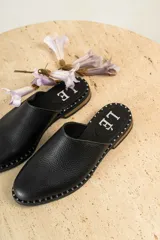 Mules de cuero negro con tachas plateadas en el borde de la suela y plantilla con logo estampado.