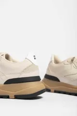 Zapatillas deportivas color crema con detalles en beige, negro y blanco.