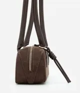 Cartera tipo shoulder bag de tamaño pequeño y formato alargado, confeccionada en material sintético efecto gamuza. Cuenta con asas de hombro estructuradas, cierre superior con cremallera y detalles metálicos decorativos.