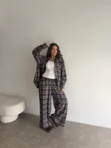 Conjunto de camisa y pantalón de viyela a cuadros en tonos marrón, blanco y azul. La camisa es oversize de manga larga con bolsillos frontales y cierre de botones. El pantalón es recto y holgado.