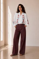 Camisa blanca de manga larga con bordados florales en tono rojo y verde en el frente y las mangas. Presenta cuello mao con escote en V y botones frontales.