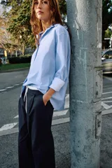 Camisa básica de algodón con cuello solapa, escote en pico y cierre frontal con botones. Presenta mangas largas con puños abotonados y bajo redondeado.