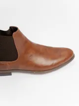 Botín tipo Chelsea de cuero sintético color marrón, con paneles elásticos laterales oscuros y suela de goma con pequeño tacón.