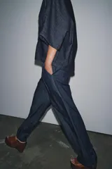 Camisa de tejido tipo denim azul oscuro, con escote pico, manga corta ancha y dos bolsillos de parche frontales. Cierre frontal con botones.