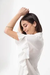 Camisa azul de corte holgado, con cuello clásico, cierre frontal con botones, mangas cortas con volados y largo hasta la mitad del muslo.