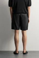 Bermuda de lino negro de corte relaxed fit, con cintura elástica ajustable mediante cordón y bolsillos frontales.