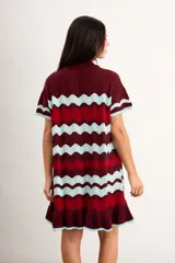 Vestido corto de punto con patrón en zigzag de franjas azules, marrones y amarillas, cuello polo con cierre frontal de un botón, mangas cortas y volado en el ruedo.