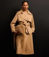 Trench coat largo de Marfinno, confeccionado en gabardina de poliéster. Presenta cuello con solapas, aletas en los hombros, cierre frontal con botones y cinta para lazo en la cintura.