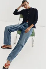 Chaqueta de punto color negro con cuello redondo, manga larga y cierre frontal con botones dorados. Presenta un corte entallado con bajo en evasé.