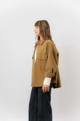 Sobrecamisa de gabardina liviana color crema, con corte oversize, cuello clásico, cierre frontal con botones a presión y dos bolsillos delanteros con solapa.