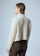 Sweater de punto grueso color crema, con cuello alto y parche circular con bordado en el pecho.